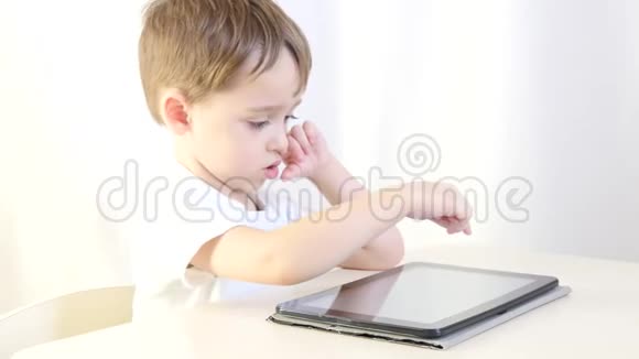 快乐的小男孩坐在桌子旁玩平板电脑特写镜头孩子在玩电子游戏因特网和视频的预览图