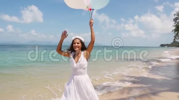 快乐的微笑美丽的新娘在热带岛屿的海滩上奔跑手里拿着气球慢动作概念视频的预览图