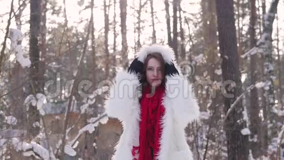 迷人的金发碧眼穿着白色的毛皮外套戴着红领巾在冬天的森林背景上摆着姿势穿白色毛皮的模特视频的预览图