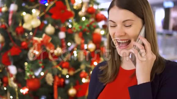 圣诞树附近的女人使用手机的漂亮女性在新年中获得祝贺视频的预览图