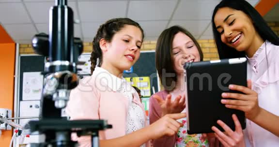 微笑的学校女生在实验室讨论数字平板电脑视频的预览图