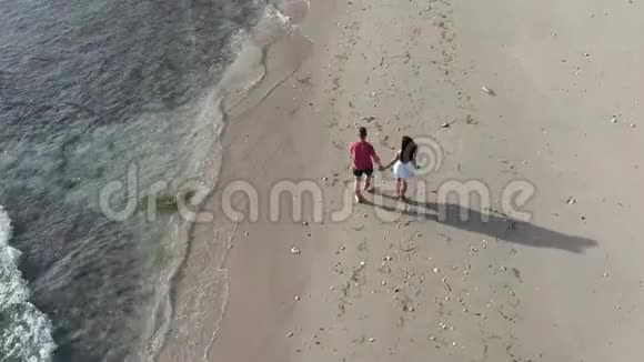 男人和女人在日落时沿着热带海滩漫步追踪年轻夫妇在度假中享受乐趣的空中镜头视频的预览图