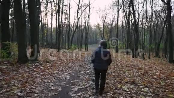 孤独的成年女子穿着温暖的秋袄走在秋林中视频的预览图