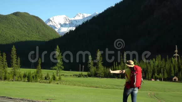 旅行者的女人带着一个红色的背包沿着路走山区阳光明媚雪山景色视频的预览图