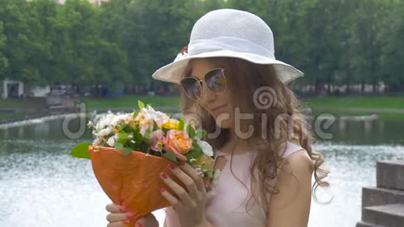 一个戴太阳镜和戴着花的白帽子的漂亮女孩的肖像特写视频的预览图