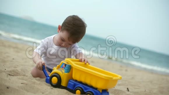 两岁漂亮的婴儿学步男孩骑着玩具货车在夏季海滩特写慢动作视频的预览图