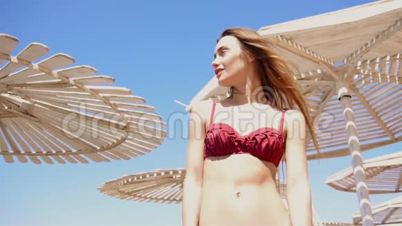 穿着泳衣的漂亮女孩站在沙滩伞上向远处望去视频的预览图