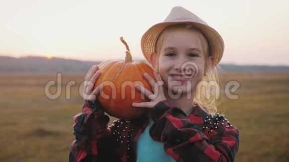 年轻的女农民戴着帽子手里拿着橙色的南瓜在日落的时候在田野里南瓜收获感恩节感恩节视频的预览图