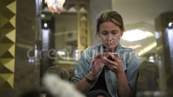 年轻的高加索女人穿着牛仔裤夹克使用智能手机在社交网络上写信息在表格中的位置视频的预览图