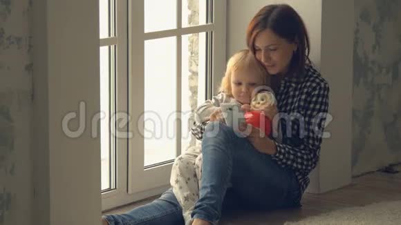 母亲和小女儿坐在靠窗的地方使用智能手机视频的预览图