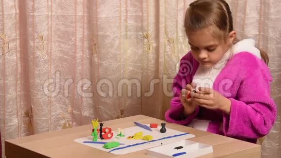 女孩坐在空地的另一边的一张桌子上用橡皮泥雕刻工艺品视频的预览图