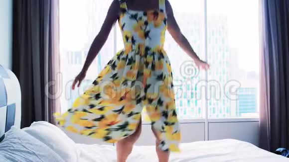 快乐的年轻女子穿着裙子跳舞在家里床上跳跃动作缓慢3840x2160视频的预览图