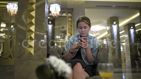 年轻的高加索女人穿着牛仔裤夹克使用智能手机在社交网络上写信息在表格中的位置视频的预览图
