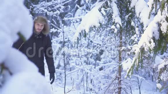 男子走雪冬季森林旅行者与背包在镜头前挥动他的手视频的预览图