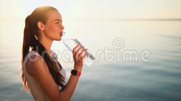 年轻的黑发女人从海边的塑料瓶里喝水视频的预览图