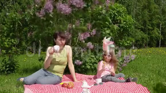 年轻的母亲和小女儿在春天的野餐旁边一朵盛开的丁香花视频的预览图