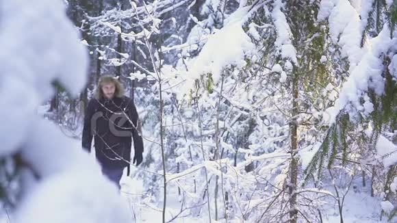 男子走雪冬季森林旅行者与背包在镜头前挥动他的手视频的预览图