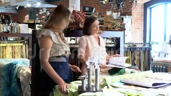 两个年轻女孩在办公室聊天妇女向顾客展示纺织品样品视频的预览图