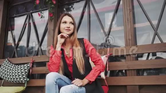 年轻漂亮的女孩穿着休闲服坐在城市公园的长凳上视频的预览图