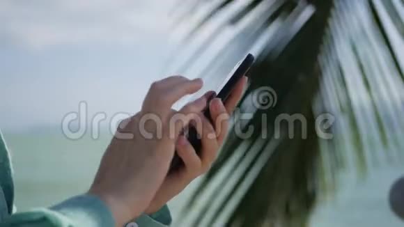 女人用智能手机在背景海和棕榈树上女孩触摸屏幕视频的预览图
