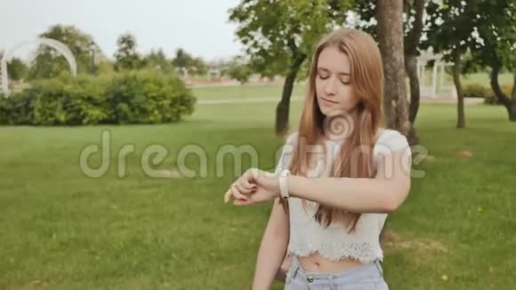 一个年轻的女孩正在公园里散步看着她手臂上的一个智能时钟接受脉搏测量视频的预览图