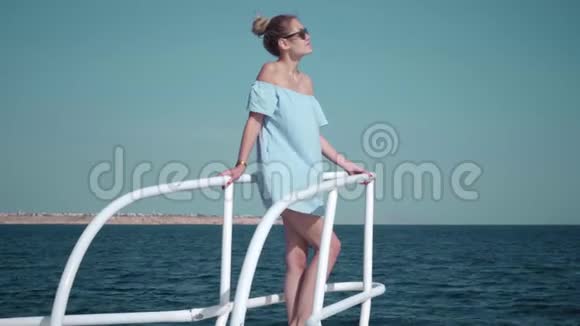 一个年轻漂亮的高加索女人在游艇上穿着蓝色连衣裙和太阳镜的肖像假期的概念视频的预览图
