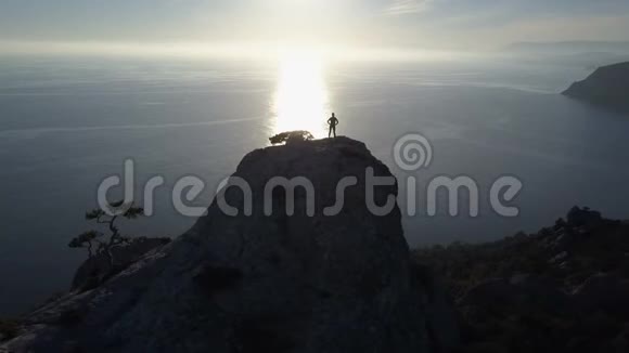 飞越一位年轻女子站在一座面向大海的山顶上在美丽的风景中登上顶峰的女士视频的预览图