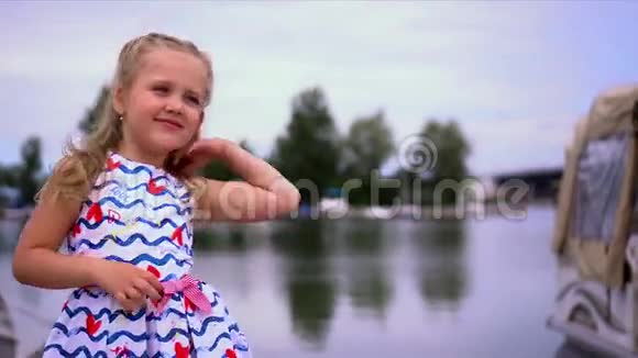 那个金发的小女孩在河边的皮尔西为照相机摆姿势视频的预览图