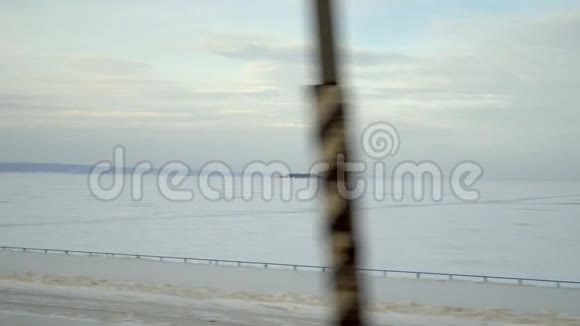 从移动的机器或火车的窗户上覆盖着冰的冬季湖泊的录像摄像机沿着海岸移动经过视频的预览图