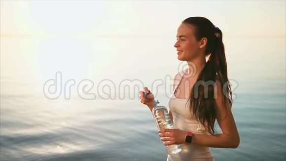 年轻运动的女人从海边的塑料瓶里喝水视频的预览图