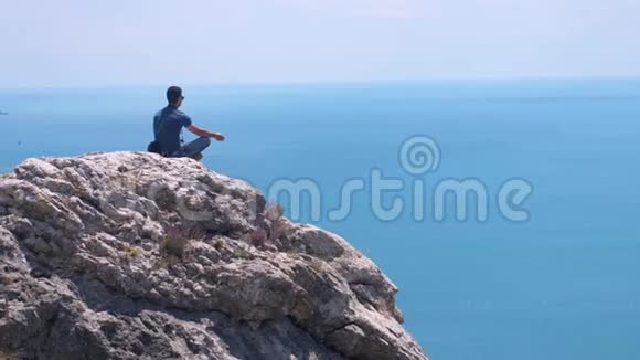 人在边上沉思坐在岩石的顶部背景是蓝色的大海和天空鸟儿在缓慢地飞翔视频的预览图