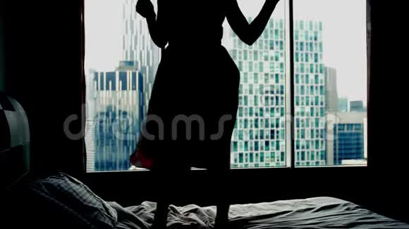 年轻快乐的女人在酒店床上跳舞的剪影慢动作3840x2160视频的预览图