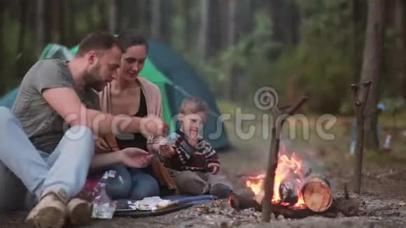 家庭在大自然中休息夫妻和他们的小儿子正在明火上煮棉花糖吃它们视频的预览图