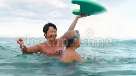 快乐的儿子和妈妈微笑着玩游泳板慢动作视频的预览图