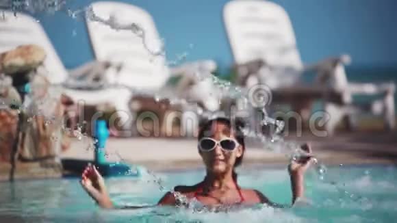 戴太阳镜的漂亮年轻女人在游泳池里放松泳池瀑布下的女人1920x1080视频的预览图