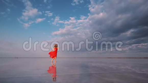 女游客穿着一件挥舞的裙子沿着一个天空反射的盐湖散步视频的预览图