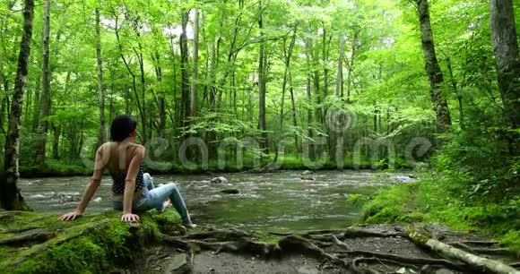 女徒步旅行者坐在深林瀑布附近视频的预览图