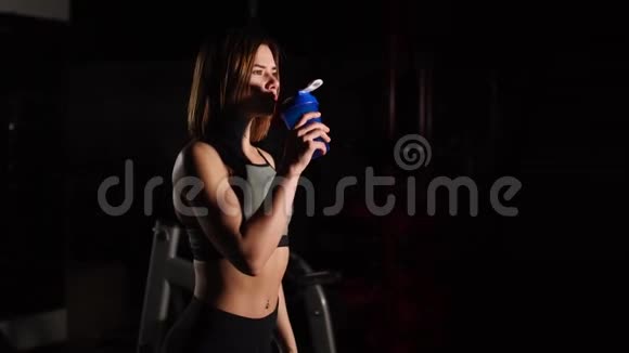 漂亮的年轻女人脖子上有一条毛巾在健身房里喝着瓶子里的水视频的预览图