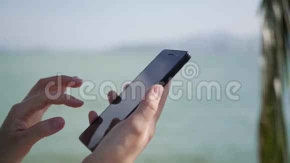 女人用智能手机在背景海和棕榈树上女孩触摸屏幕视频的预览图