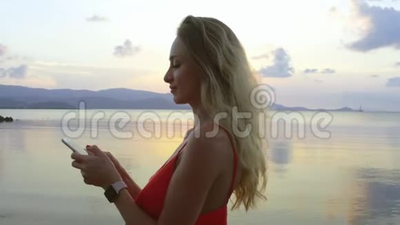 美丽的女人在海滩上的智能手机上发短信视频的预览图