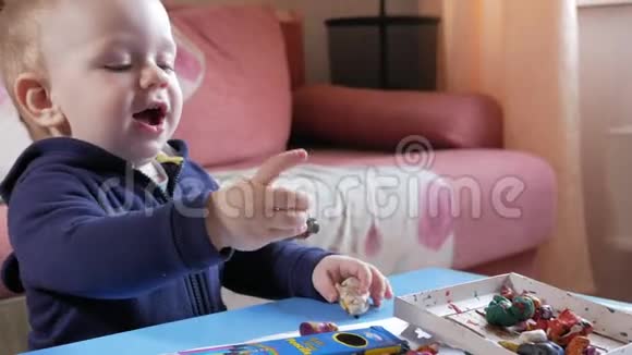 一个有魅力的男孩2岁他在家里的一张桌子上用一种多色的塑料制品塑造自己结果发现视频的预览图