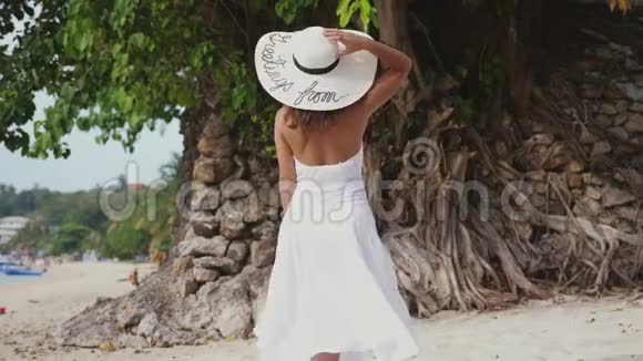 年轻的黑发女人穿着白色的衣服和帽子在热带海滩上奔跑慢动作3840x2160视频的预览图