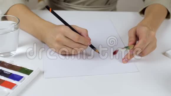 无法辨认的女人在复活节卡片上画了一个铅笔素描桌子上摆着一个颜料调色板和一杯视频的预览图