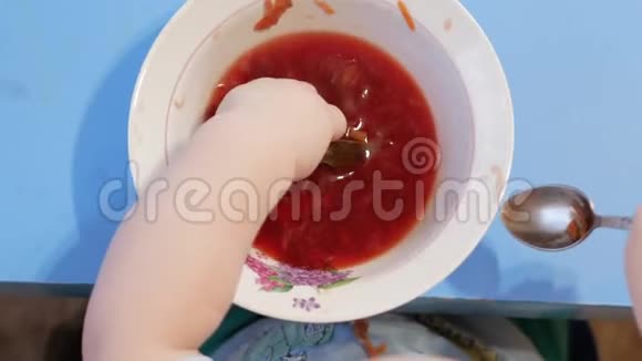 一个2岁有魅力的男孩自己在吃红汤他把手伸进盘子里桌面视图视频的预览图