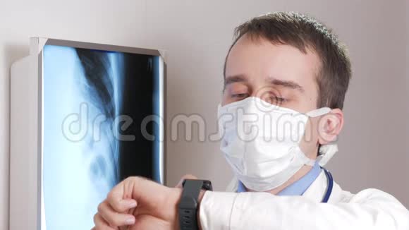 一位戴面膜的年轻医生在诊所里使用一只智能手表这个人告诉病人x光结果视频的预览图