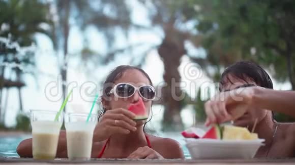 快乐的年轻夫妇戴着太阳镜度假时在游泳池里吃水果1920x1080视频的预览图