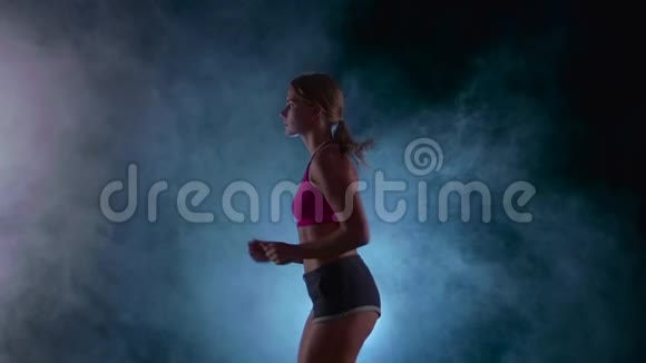 运动健身女孩在黑色背景上奔跑被烟雾中的聚光灯照亮慢动作关门视频的预览图