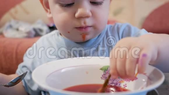 一个2岁有魅力的男孩自己在吃红汤贝叶夹在盘子里孩子玩它视频的预览图