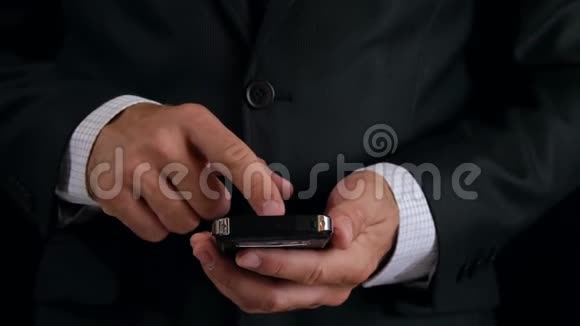 一个穿黑色西装的商人在网上工作一个男人的手拿着一部黑色背景的时尚手机视频的预览图