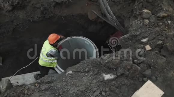 工人戴安全帽在沟内拧下混凝土房人孔环的金属绳视频的预览图